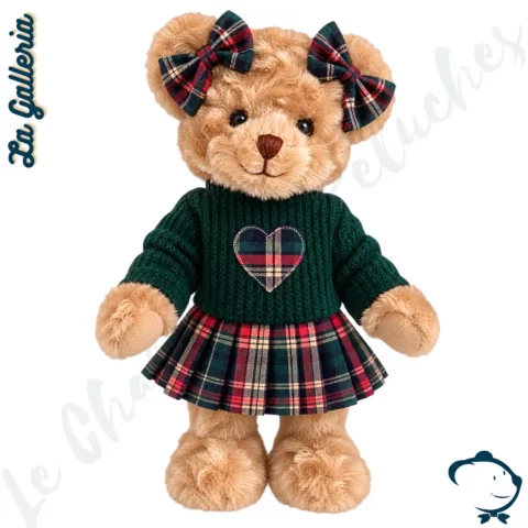 Fiona, oursonne en peluche La Galleria de 30 cm au pelage blond caramel, vêtue d'un pull vert sapin, d'une jupe écossaise et de nœuds tartan assortis.